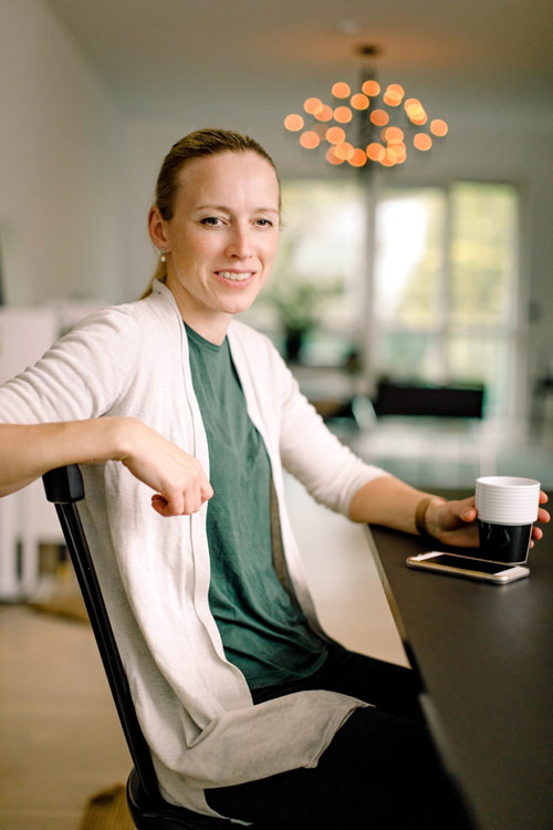 Annika sitter vid ett skrivbord med en kopp kaffe i handen.