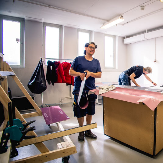 Två personal på Eventgaraget arbetar med foliering i en ljus och luftig lokal.